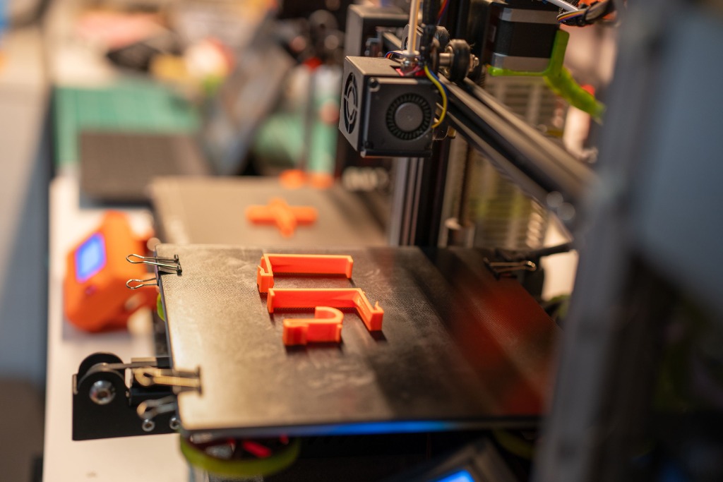 Impresora 3D fabricando piezas capa a capa en filamento naranja
